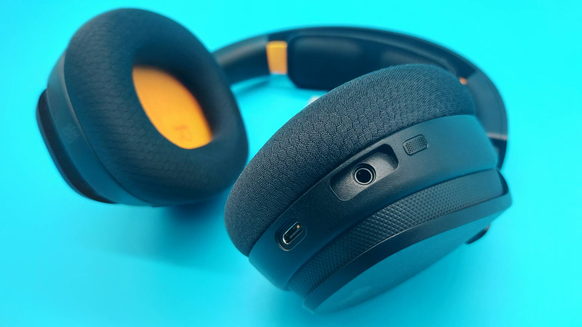 The GHS Wireless InfinitePlay seen from various angles on a blue background. This is a wireless gaming headset from Glorious. It is black all over, save for a few subtle orange accents.