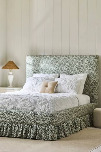 A cozy, patterned bed with a high headboard, quilted bedding, and a bedside lamp on a nightstand in a well-lit bedroom