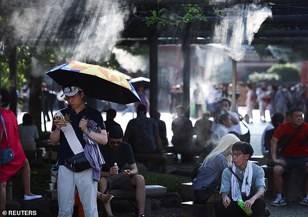 This comes as Japan faces a heatwave that has sent temperatures soaring to 38°C (100°F), sending 4,500 people to hospital with heatstroke symptoms. Pictured: People in Tokyo seek shelter under a cooling mist