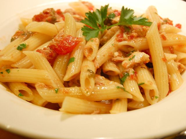 close up view of Pasta with Tuna and Tomato Sauce garnished with fresh herbs in a white bowl