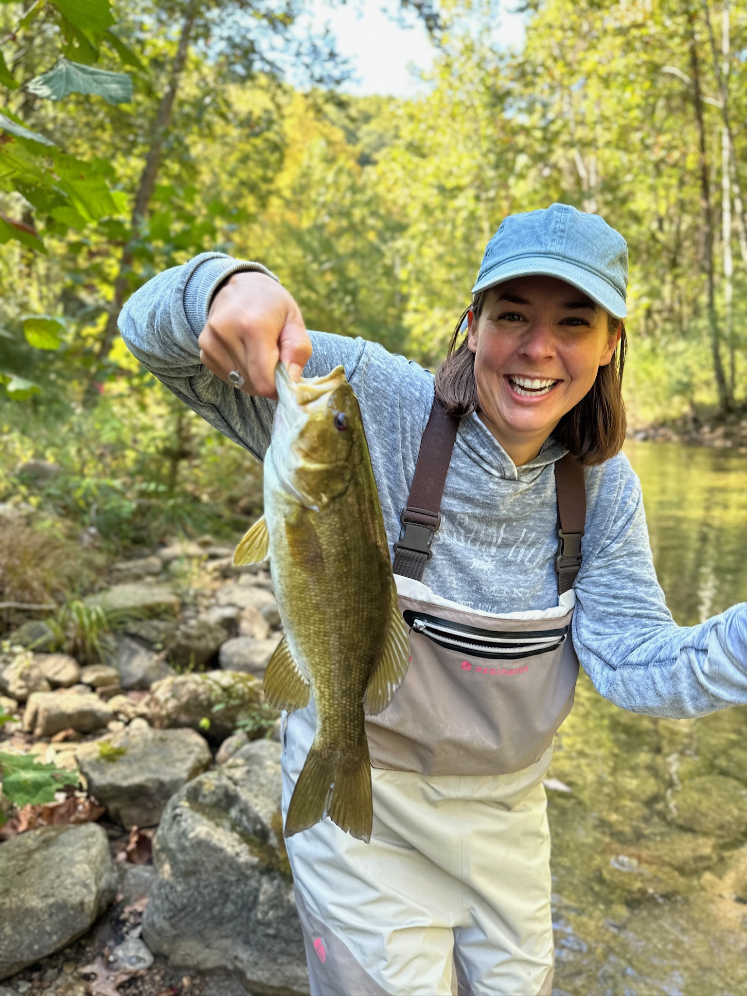 A woman holds up a nice smallmouth bass caught on the fly while wading.
