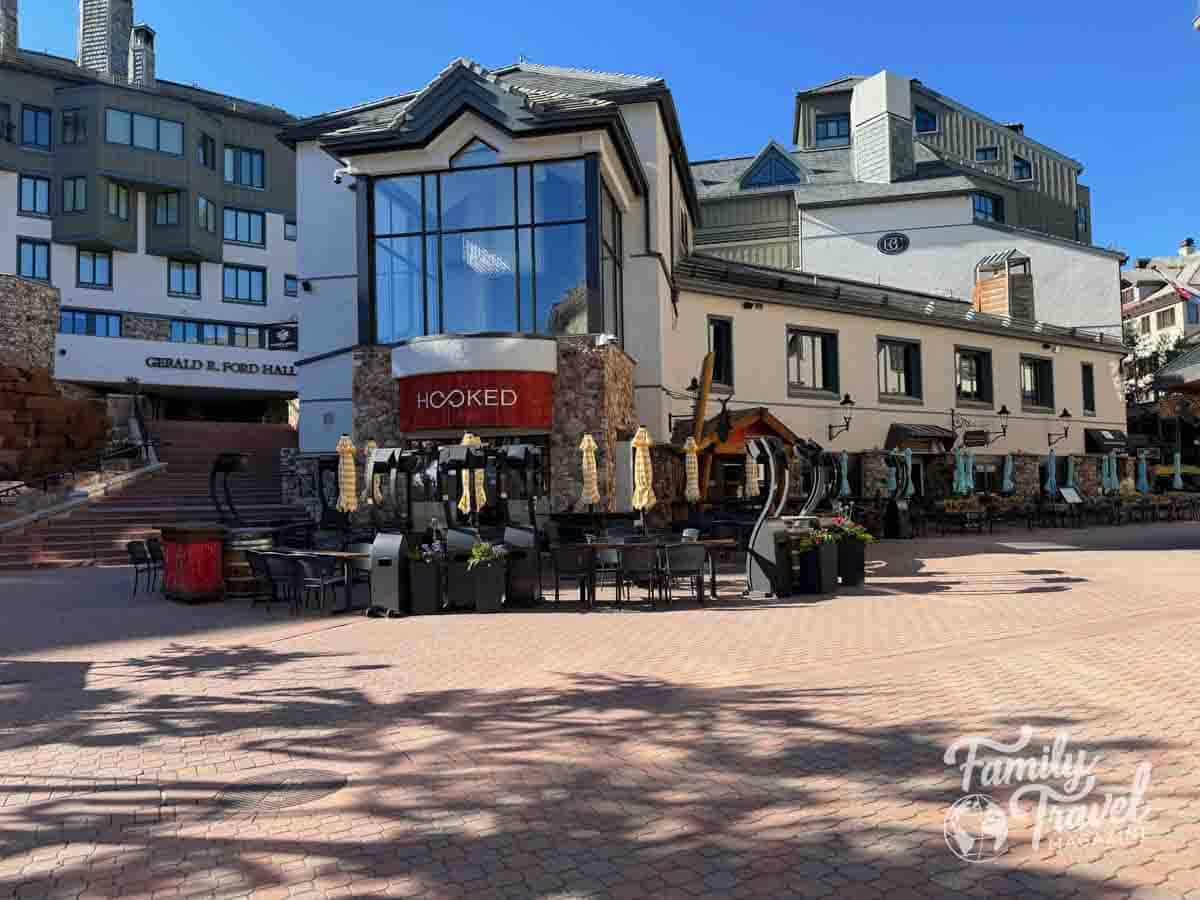 Gerald R. Ford Hall and Hooked restaurant in Beaver Creek, Colorado, with outdoor seating on a sunny day.