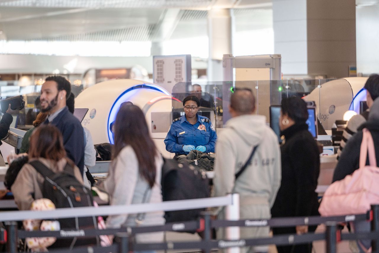 People in line at an airport security checkpoint TSA agent operating a scanner