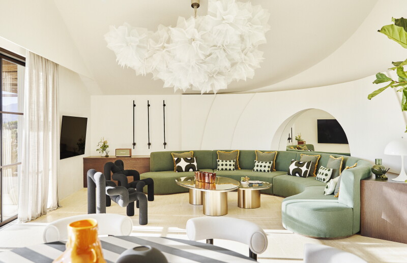 Hotel lobby interior with a curved green modern couch, cream-colored walls, and gold oval coffee tables