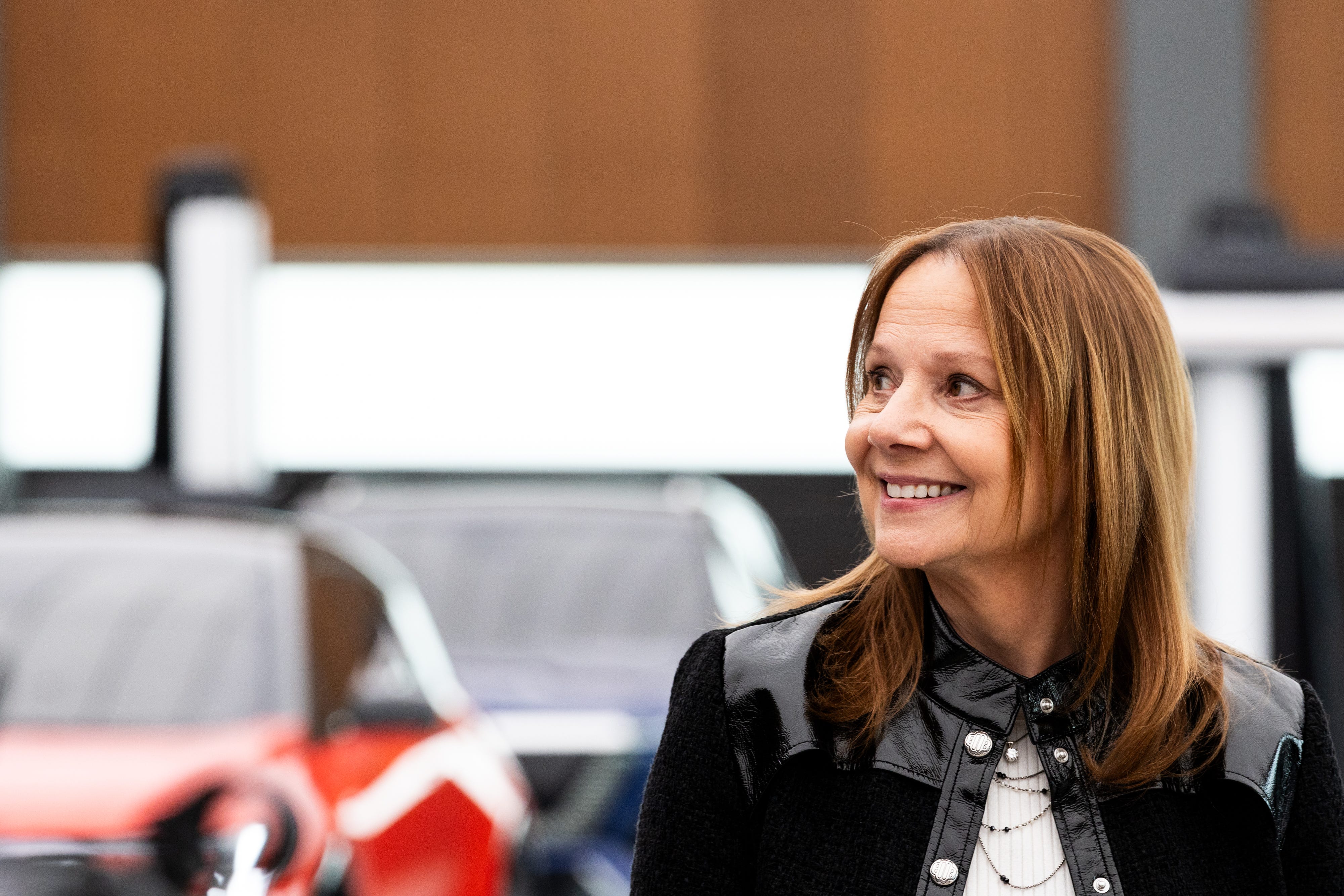 Mary Barra, GM's CEO and chair, looks to her right. In the background, there are two Cadillac EVs: the Optiq and Vistiq.
