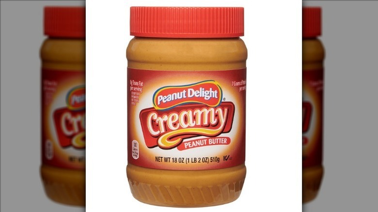 Peanut delight creamy peanut butter in a plastic jar with a red lid on a white background.