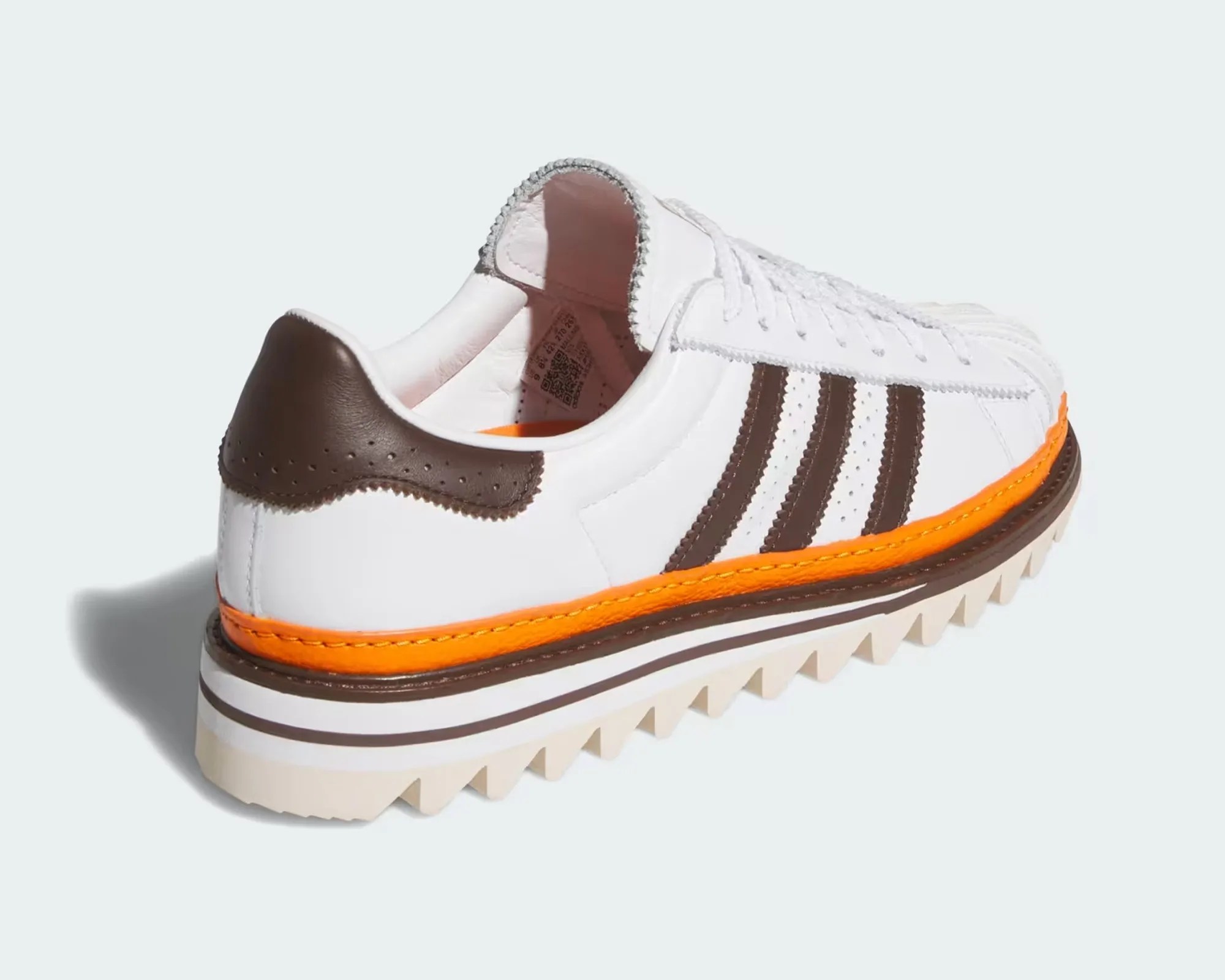 White sneaker with brown heel and stripes, orange midsole detail, and jagged cream outsole.