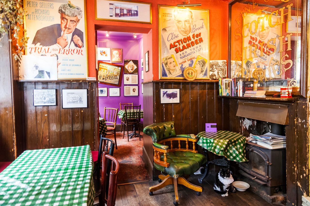 Interior of a pub with posters on the walls wooden furniture checkered tablecloths and a blackandwhite cat near a stove
