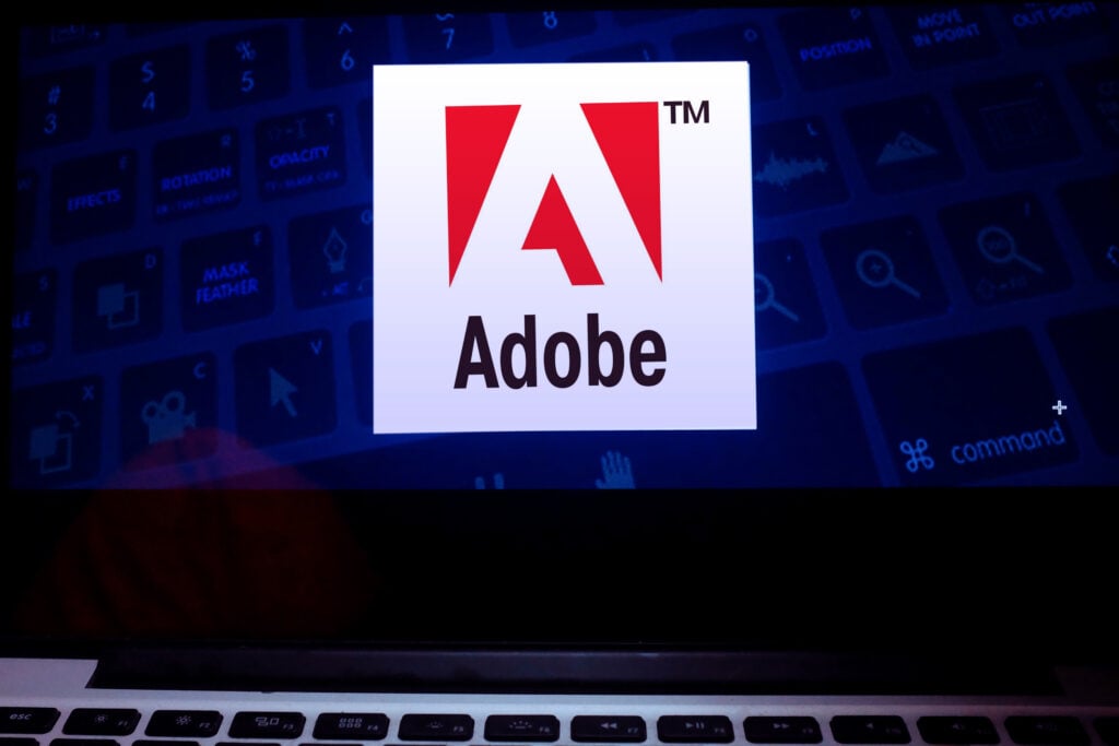 Adobe logo on a laptop screen showing a dark blue software interface with editing controls.