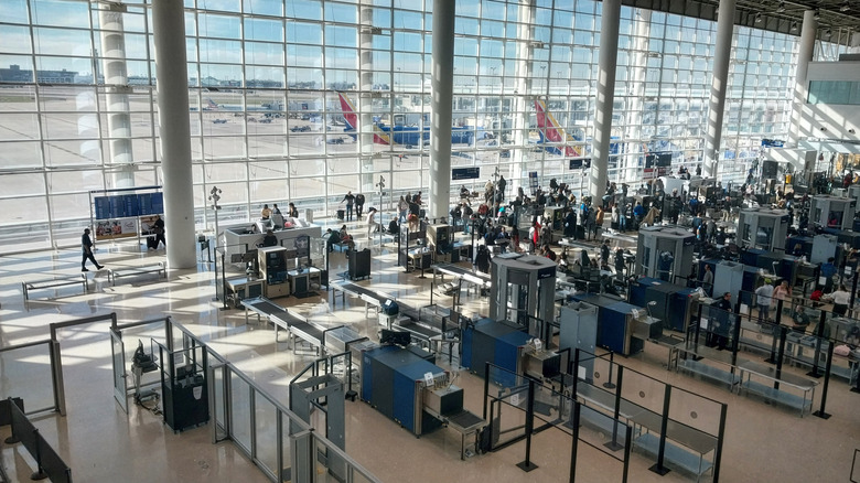 Security machines at a TSA security check point with planes on the tarmac through a window in the background