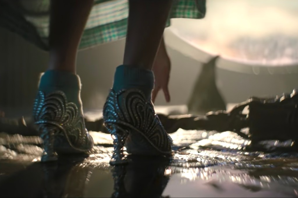 Person wearing elaborate, patterned shoes with high heels walking on a reflective surface.
