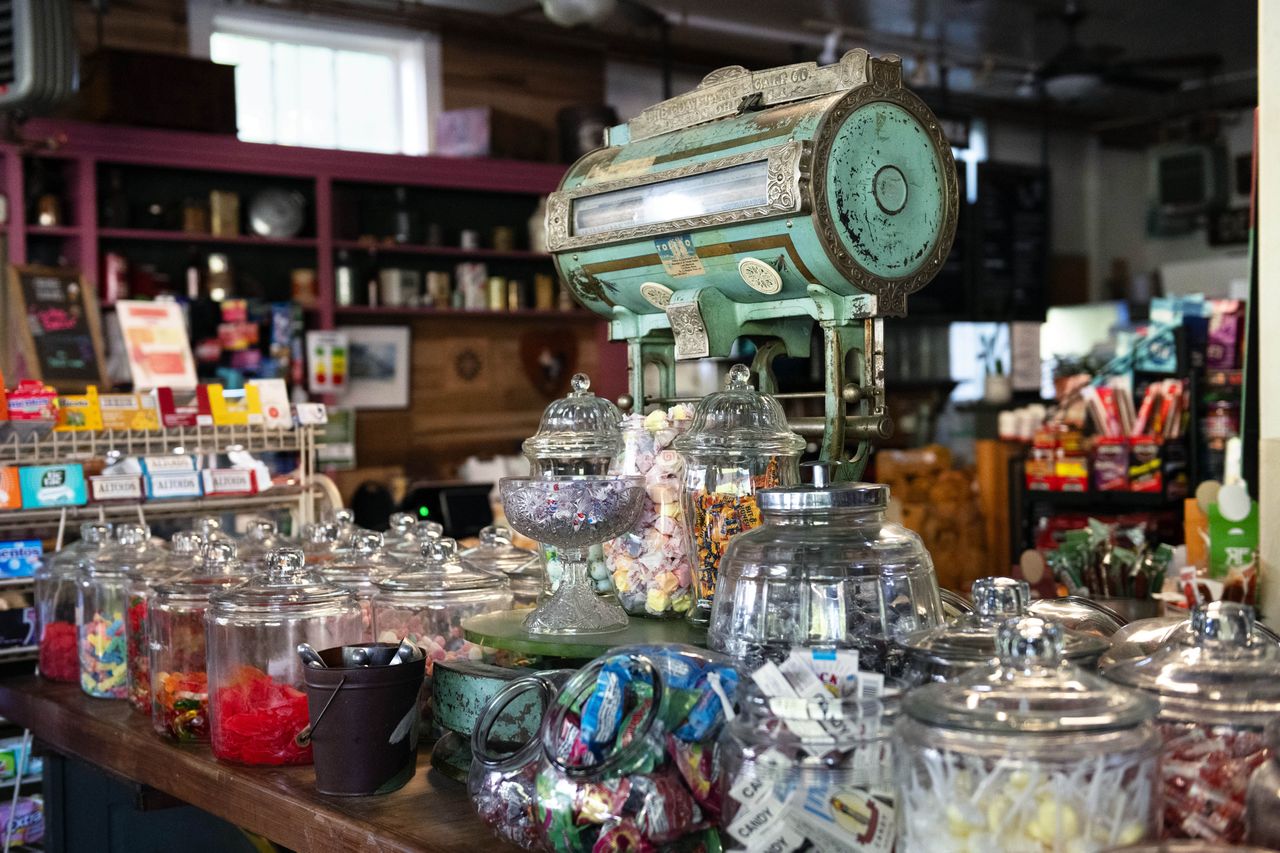 A display of candy jars and an antique scale in a small country store setting featuring various types of sweets and vintage decor
