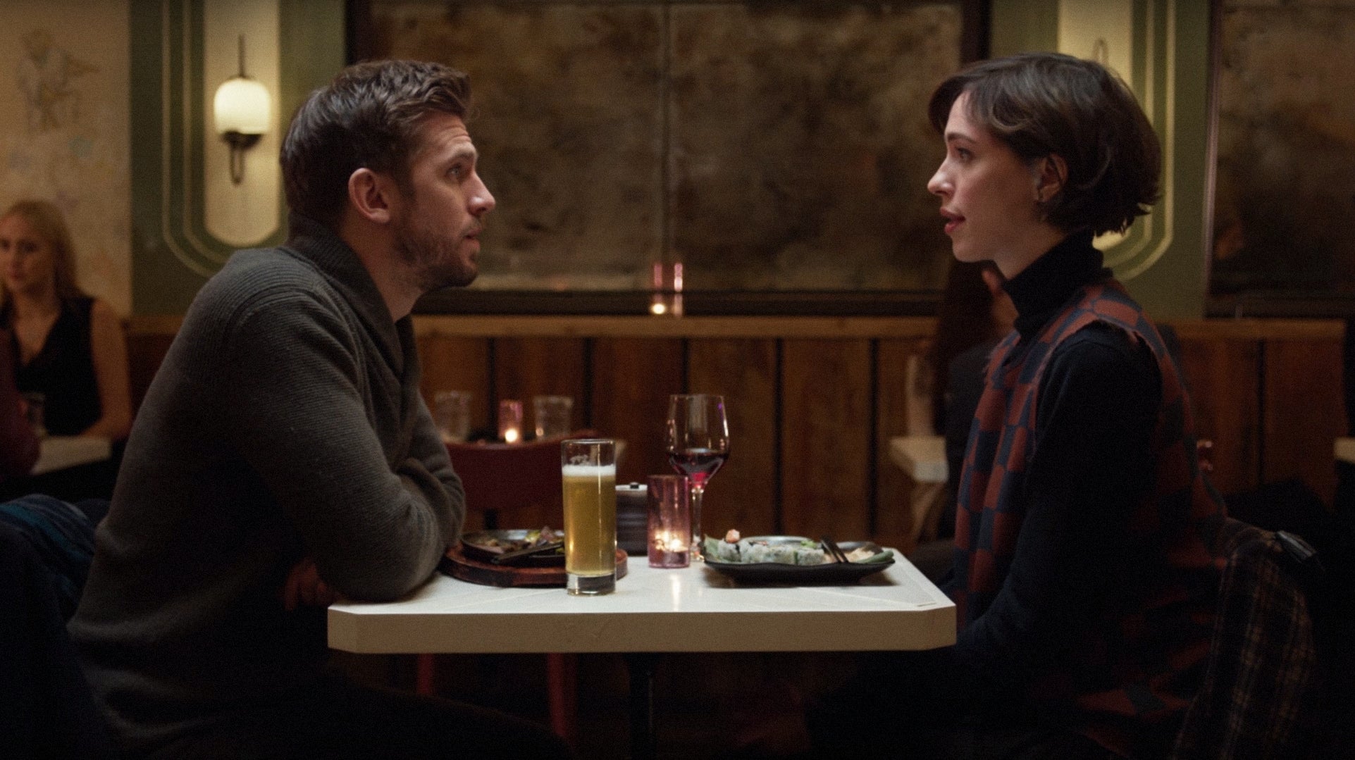A couple sits at a restaurant table facing each other, engaging in conversation over dinner and drinks