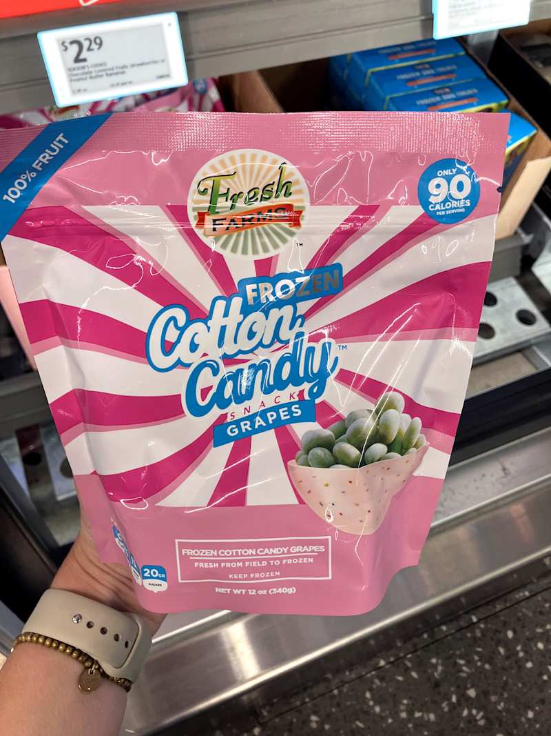 Frozen cotton candy grapes in a pink bag with colorful design, held in hand, priced at $2.29.