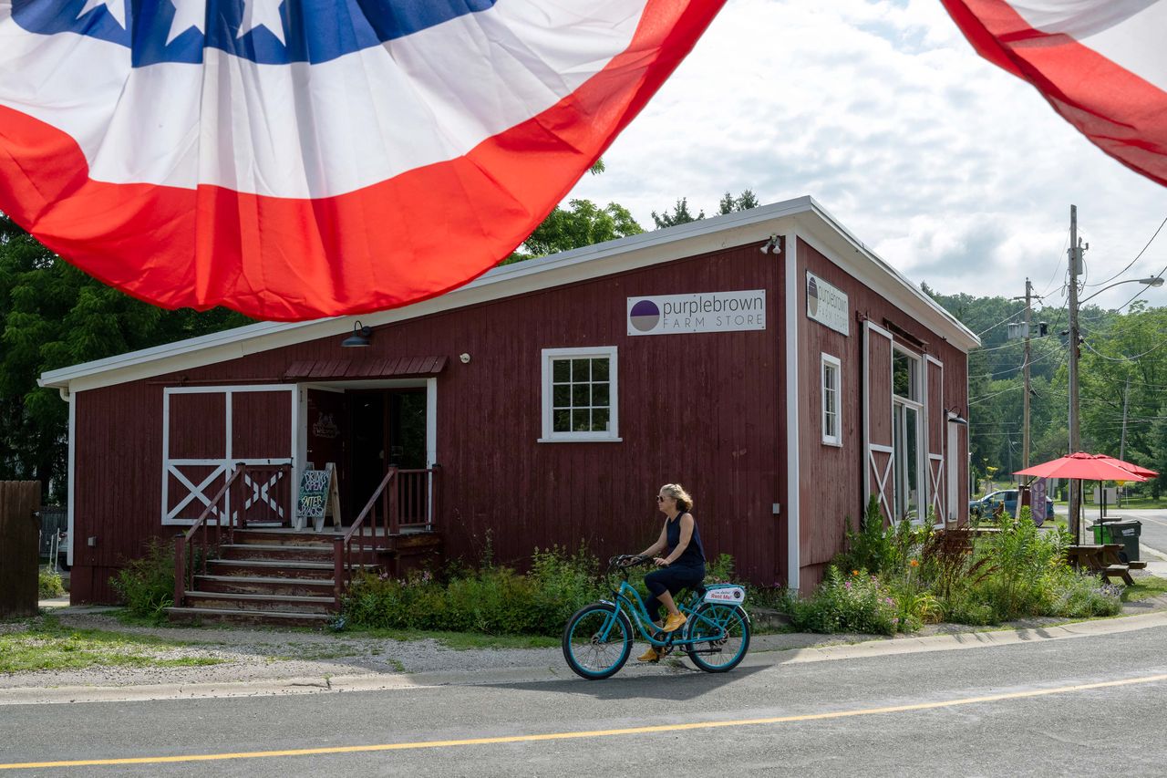 A person riding a bike past Purplebrown Farm Store decorated with bunting