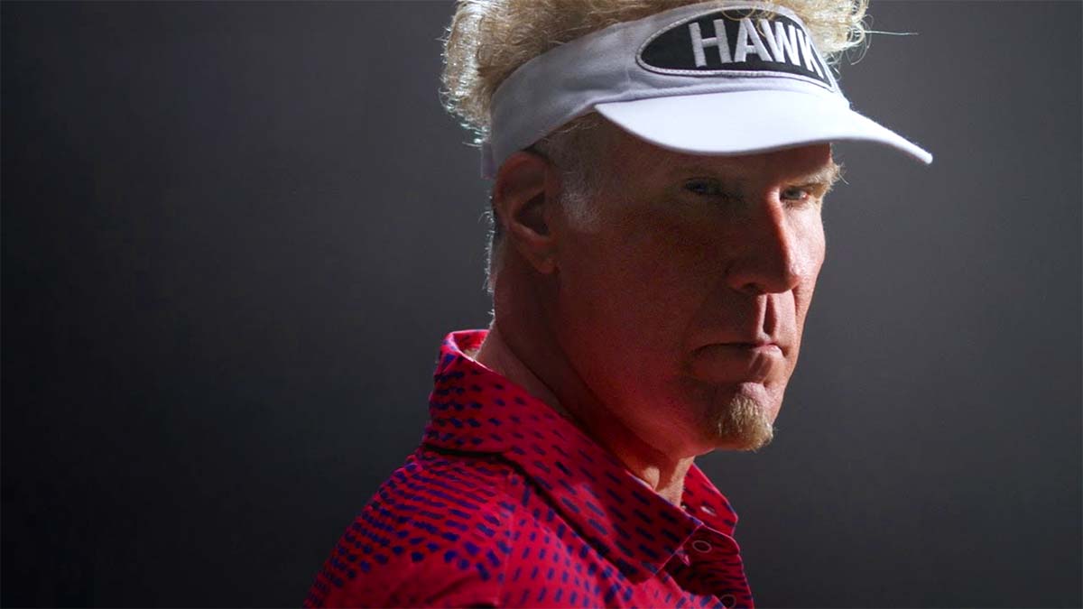A man wearing a golf visor and red shirt looks sternly at the camera