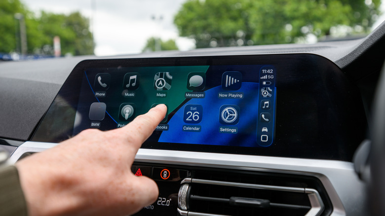 Close-up of a hand interacting with Apple CarPlay interface inside a car.