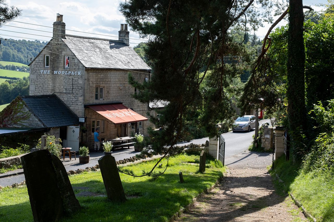 The Woolpack pub on a countryside road with surrounding trees and gravestones