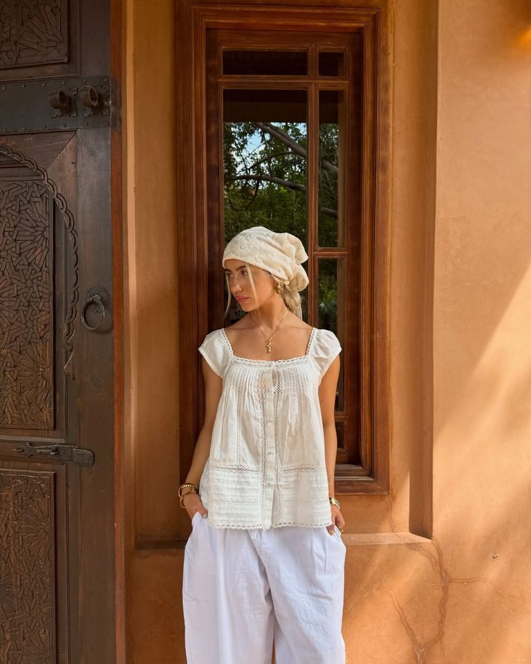 Person standing outside near a wooden window wearing a headscarf and casual attire gazing to the side