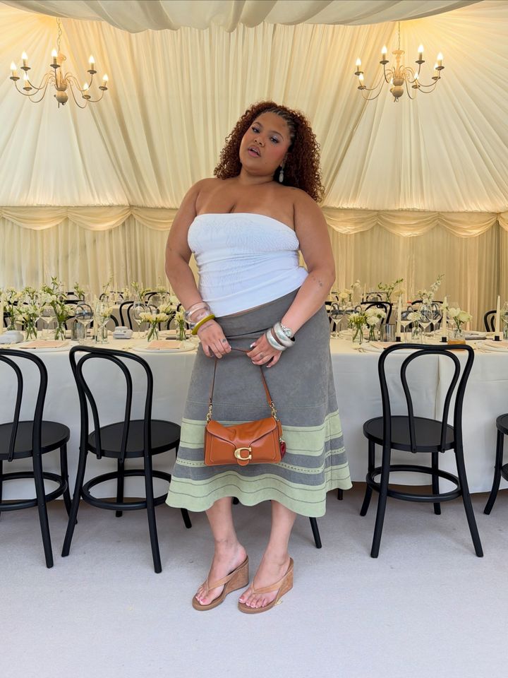 A woman standing in a decorated tent holding a handbag with a table and chairs in the background