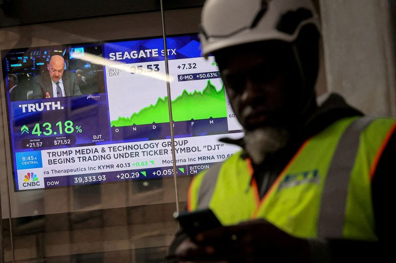 FILE PHOTO: A man looks at this phone as a screen displays trading information about shares of Truth Social and Trump Media & Technology Group in New York