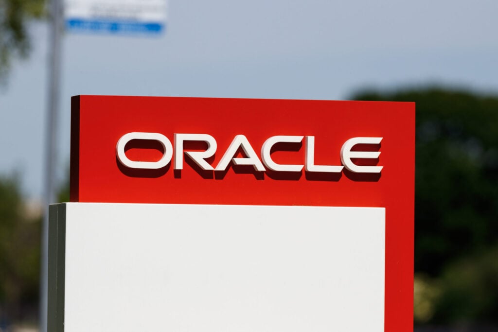An outdoor sign displays the white, raised ORACLE logo on a red background, with a blank white section below.