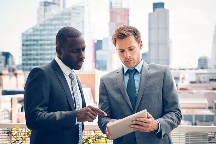 Two people in suits reviewing a document while buildings loom in the background.