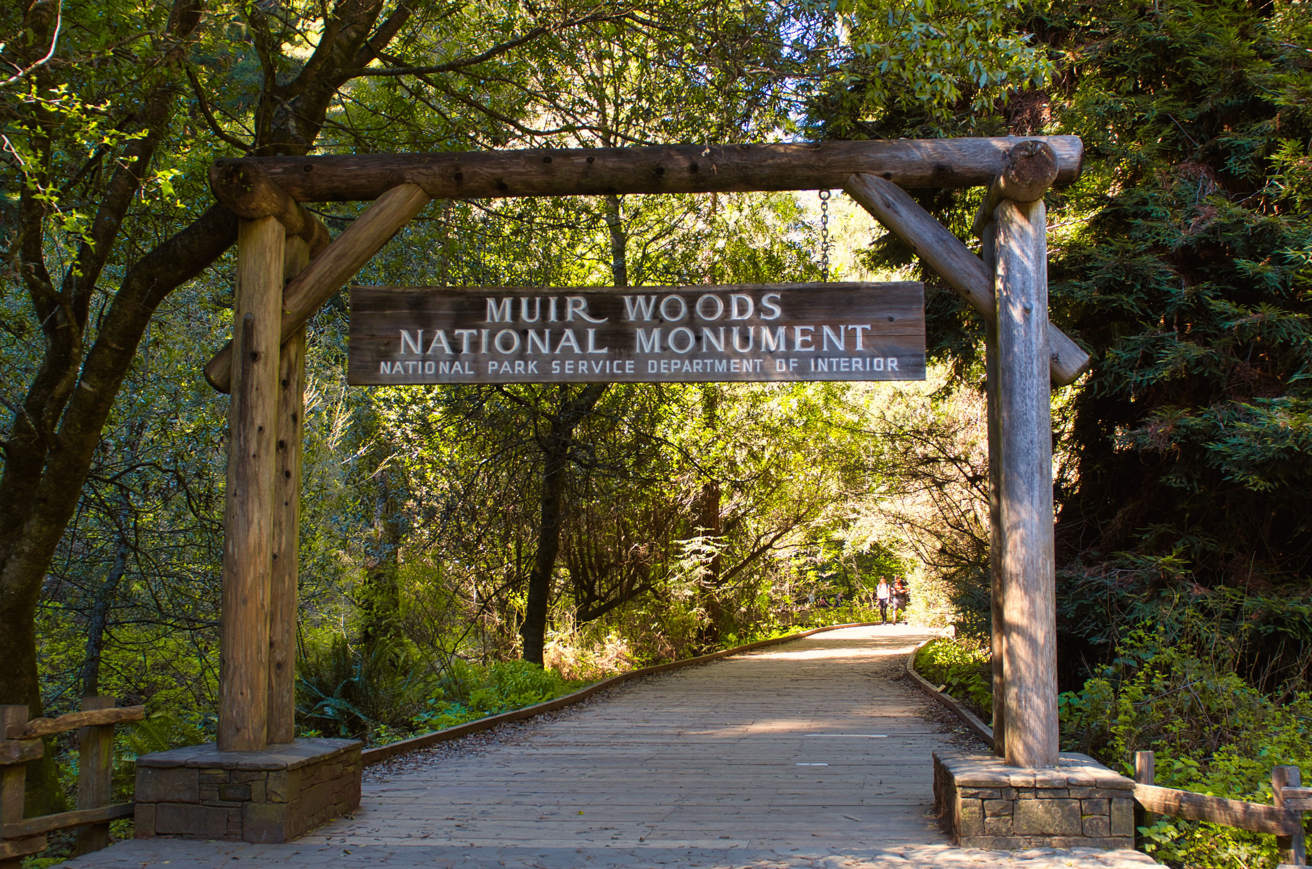 Entrance sign to Muir Woods National Monument with a wooden walkway leading into a dense forest