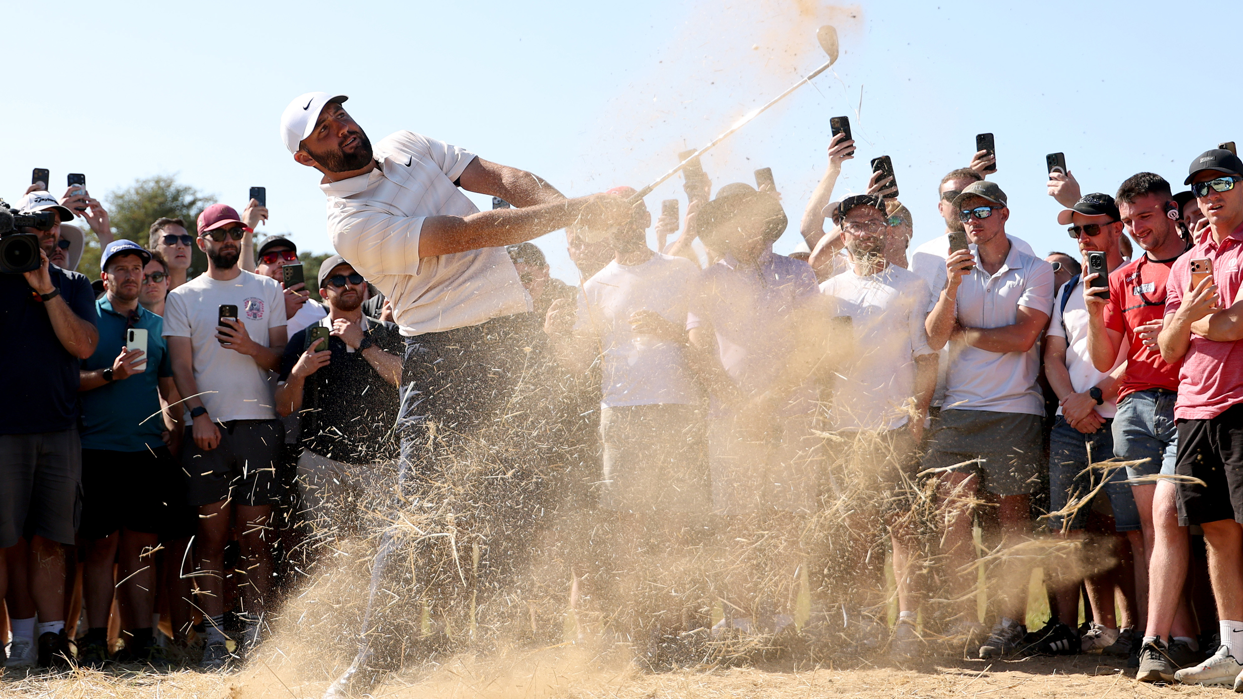 Scottie Scheffler following impact on a sandy wedge shot in front of crowds at The Open