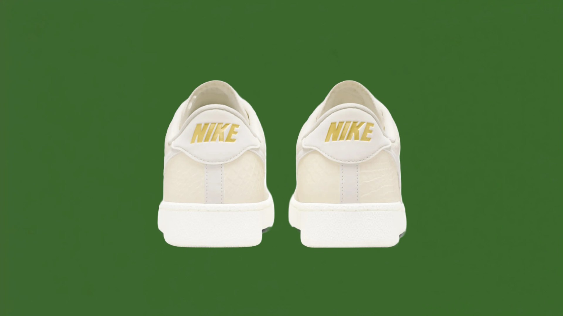 Pair of off-white Nike sneakers with gold Nike logos on the heel against a green background.