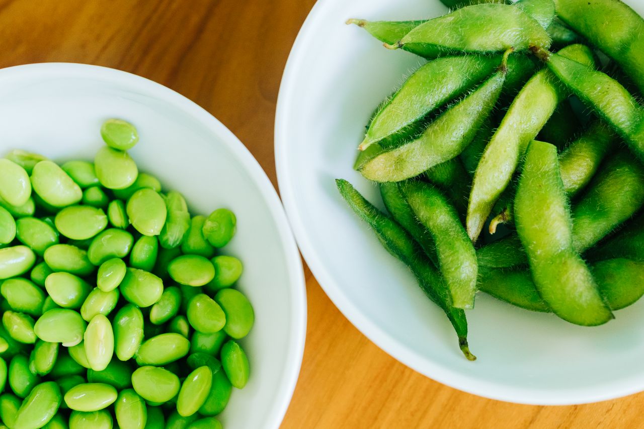 Two bowls one with shelled edamame and one with edamame pods