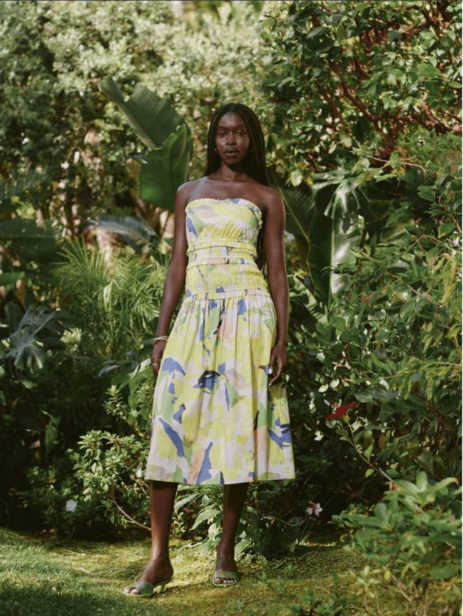 Person wearing a strapless, patterned midi dress stands in a lush garden setting