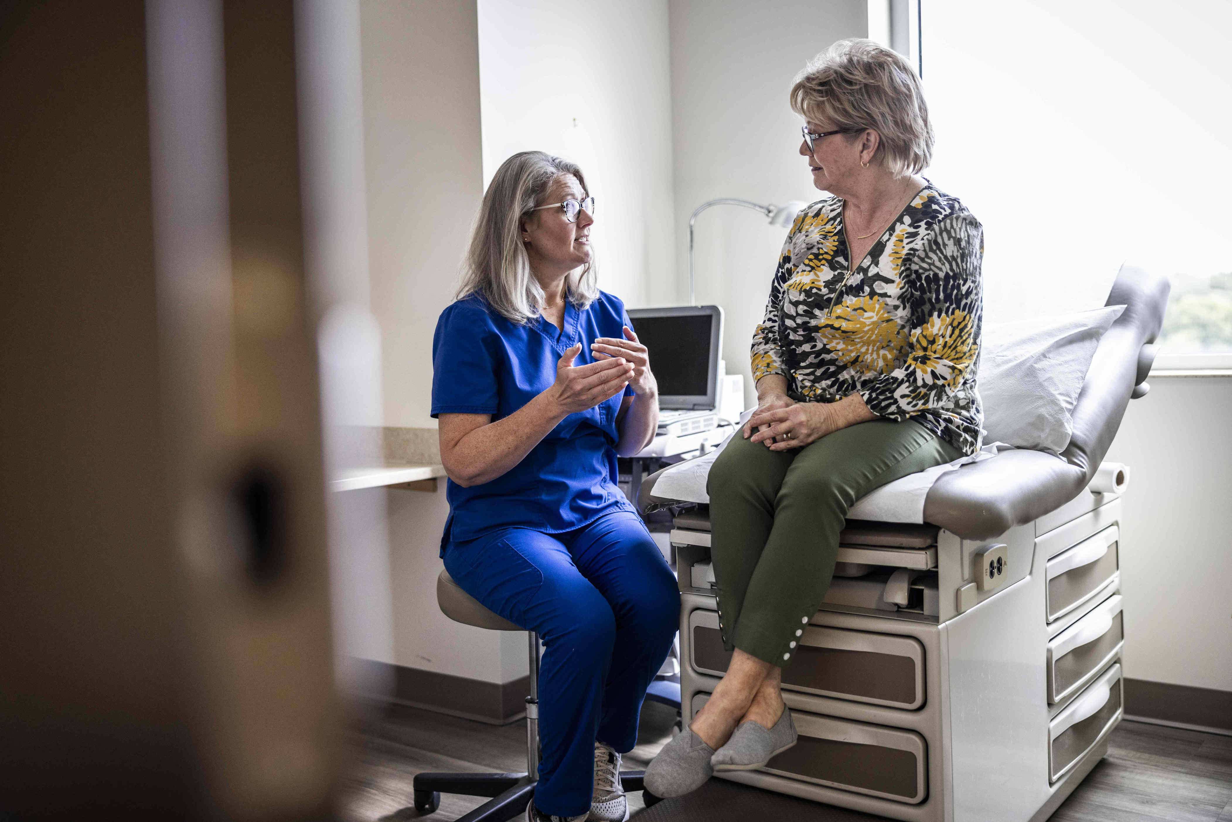 A healthcare professional speaking with a patient seated on an examination table