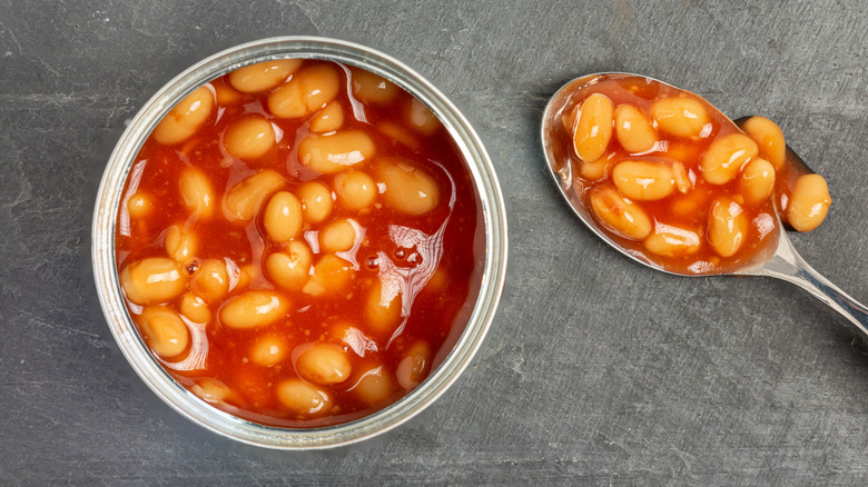 An open can of baked beans sits on a counter with a spoon of baked beans next to it
