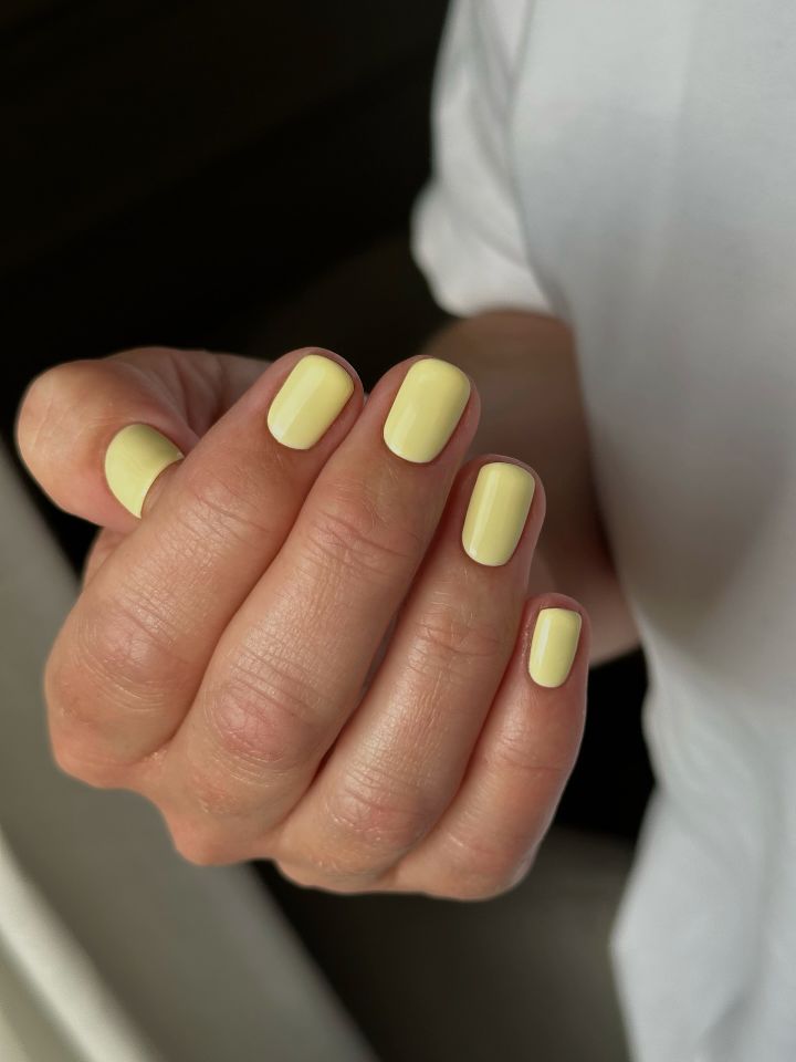 A hand with neatly manicured fingernails short and painted in a light yellow against a neutral background