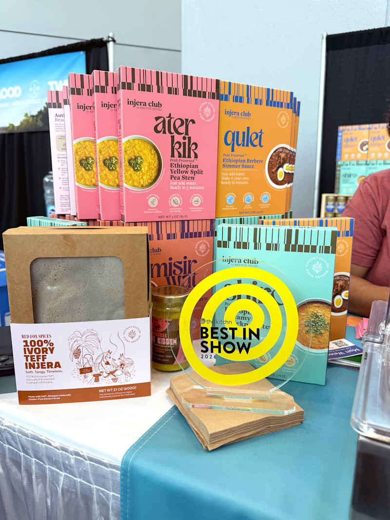 Colorful packaging of Ethiopian food products, including stews and injera, displayed at a trade show with a