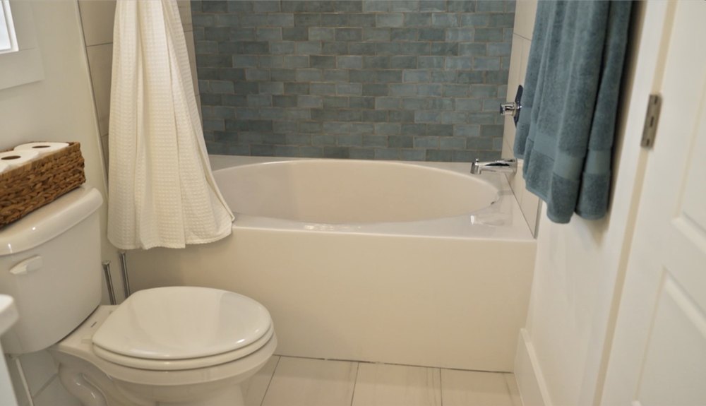 The house tour also leads to a bathroom with white plumbing features and blue subway-tiled walls.