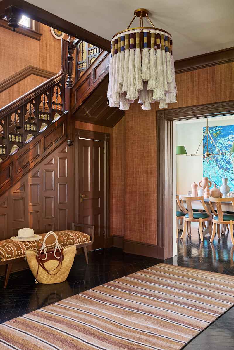 Entryway featuring a wooden staircase, a decorative chandelier, a patterned bench, and a striped rug.