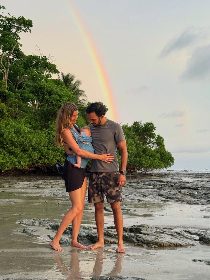 A couple with a baby standing on a beach under a rainbow