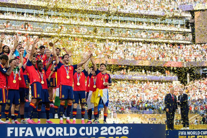 Soccer team celebrates winning FIFA World Cup 2026 on stage with trophy, surrounded by falling confetti and cheering crowd in background