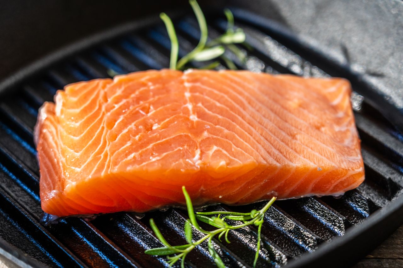 A salmon fillet on a grill pan with sprigs of herbs