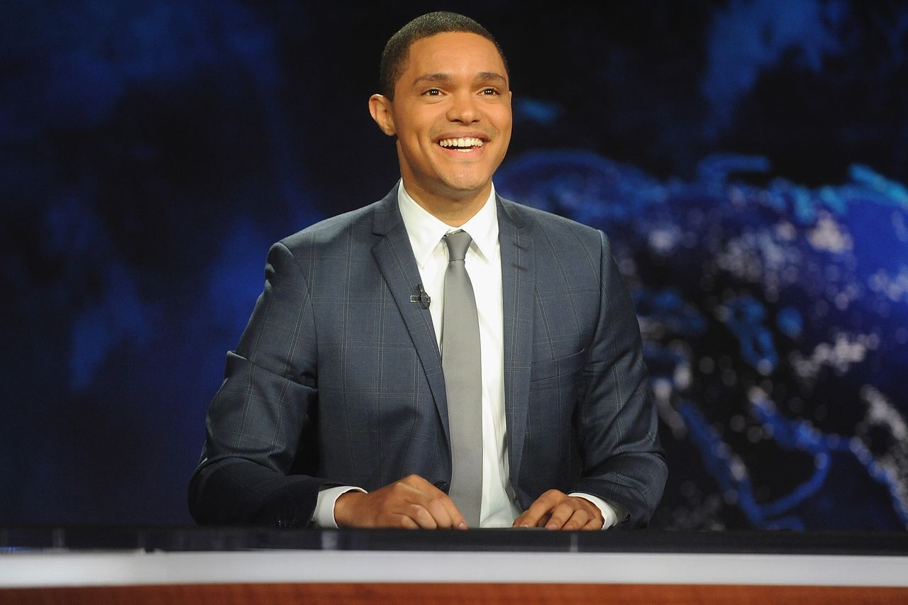 Trevor Noah seated at a desk smiling