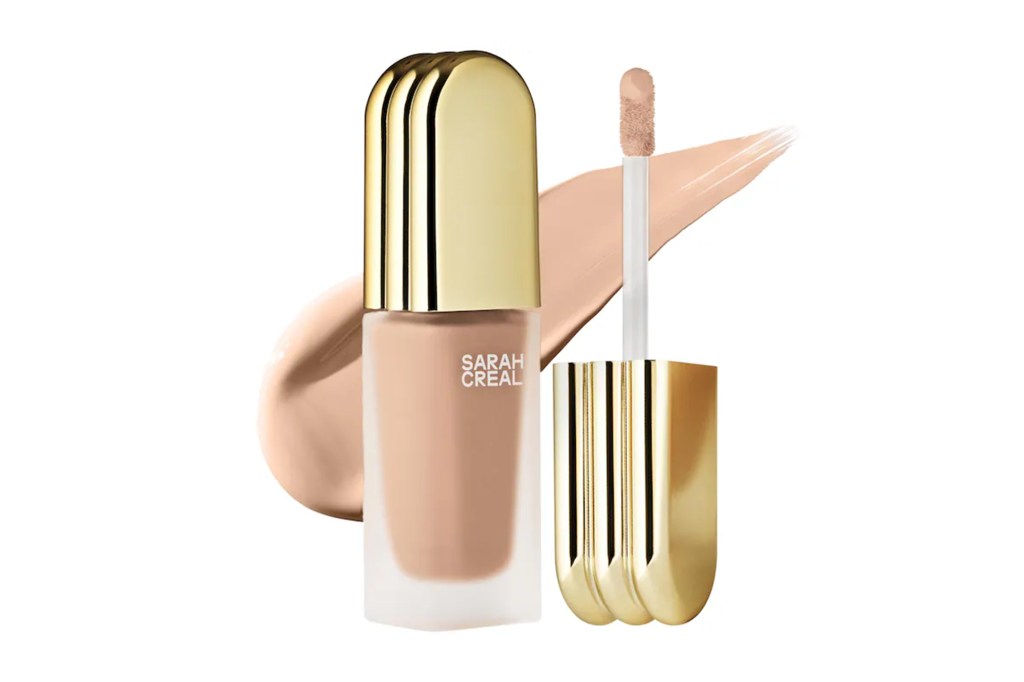 Sarah Creal liquid foundation in a frosted bottle with a golden cap and applicator, with a swatch of the foundation.