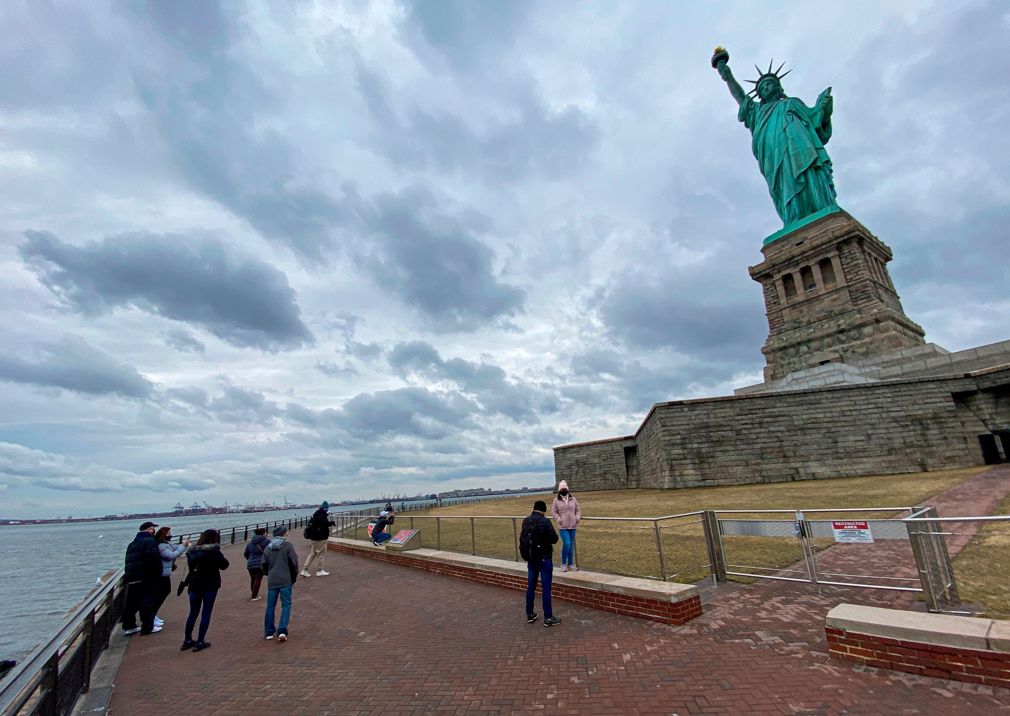 People taking photos near the Statue of Liberty on a cloudy day