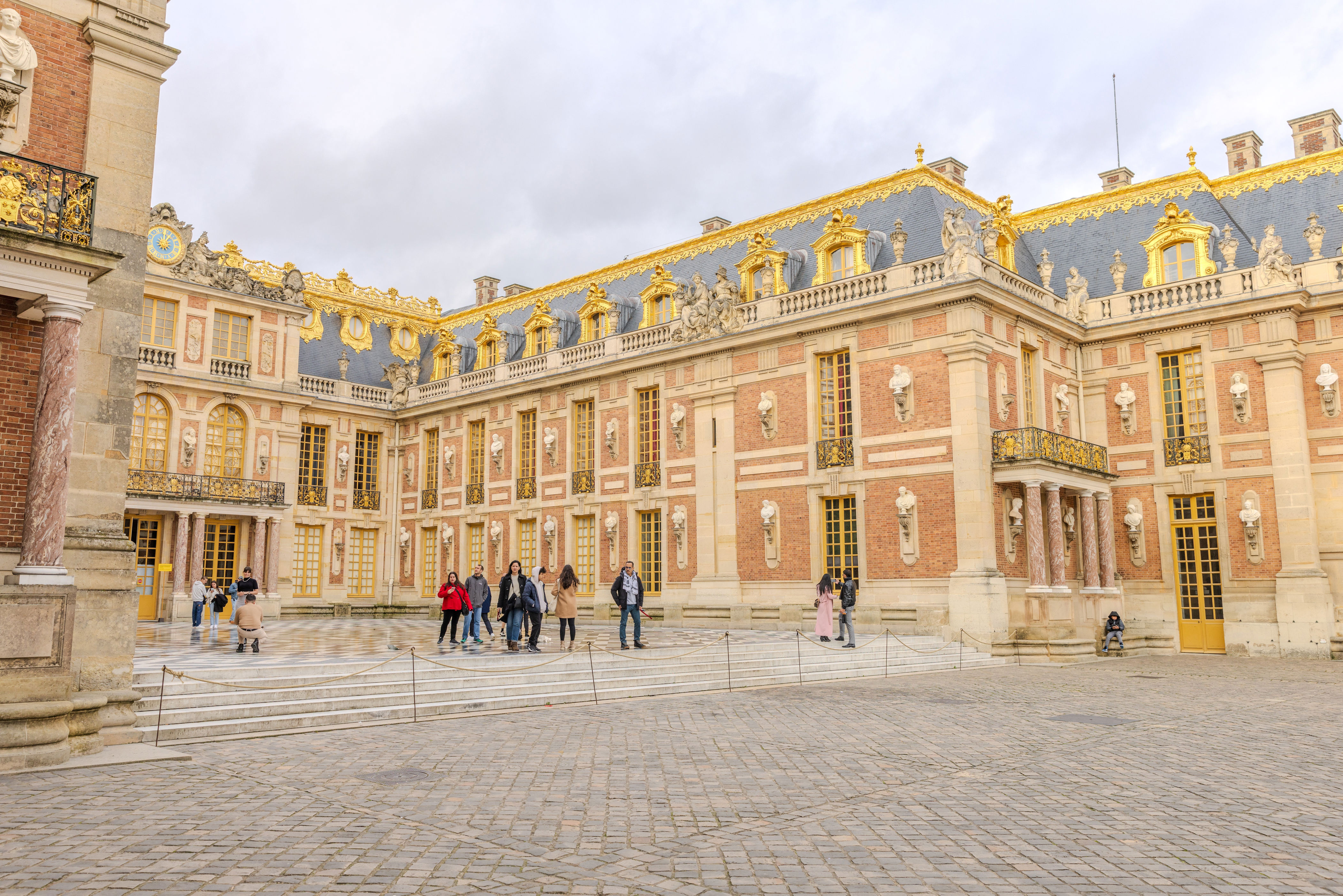 People touring the Palace of Versailles' grand exterior with ornate gold accents and majestic architecture