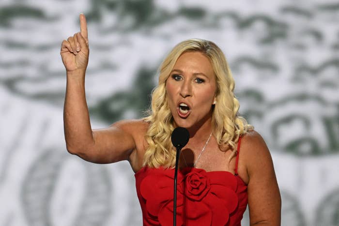 Person in red dress passionately speaking on stage, gesturing with raised finger