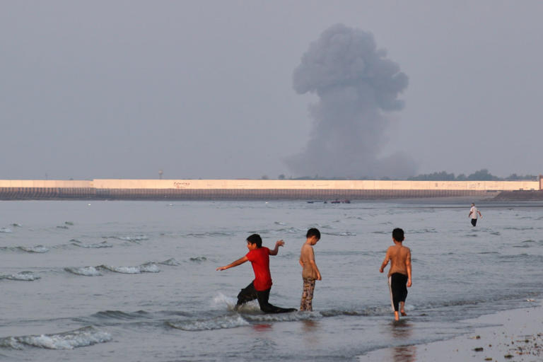 Boys play in the waters of the Strait of Hormuz as smoke rises in the background off Bandar Abbas, Iran. Most Japanese crude oil imports from the Middle East are shipped through the waterway. Photo: AP