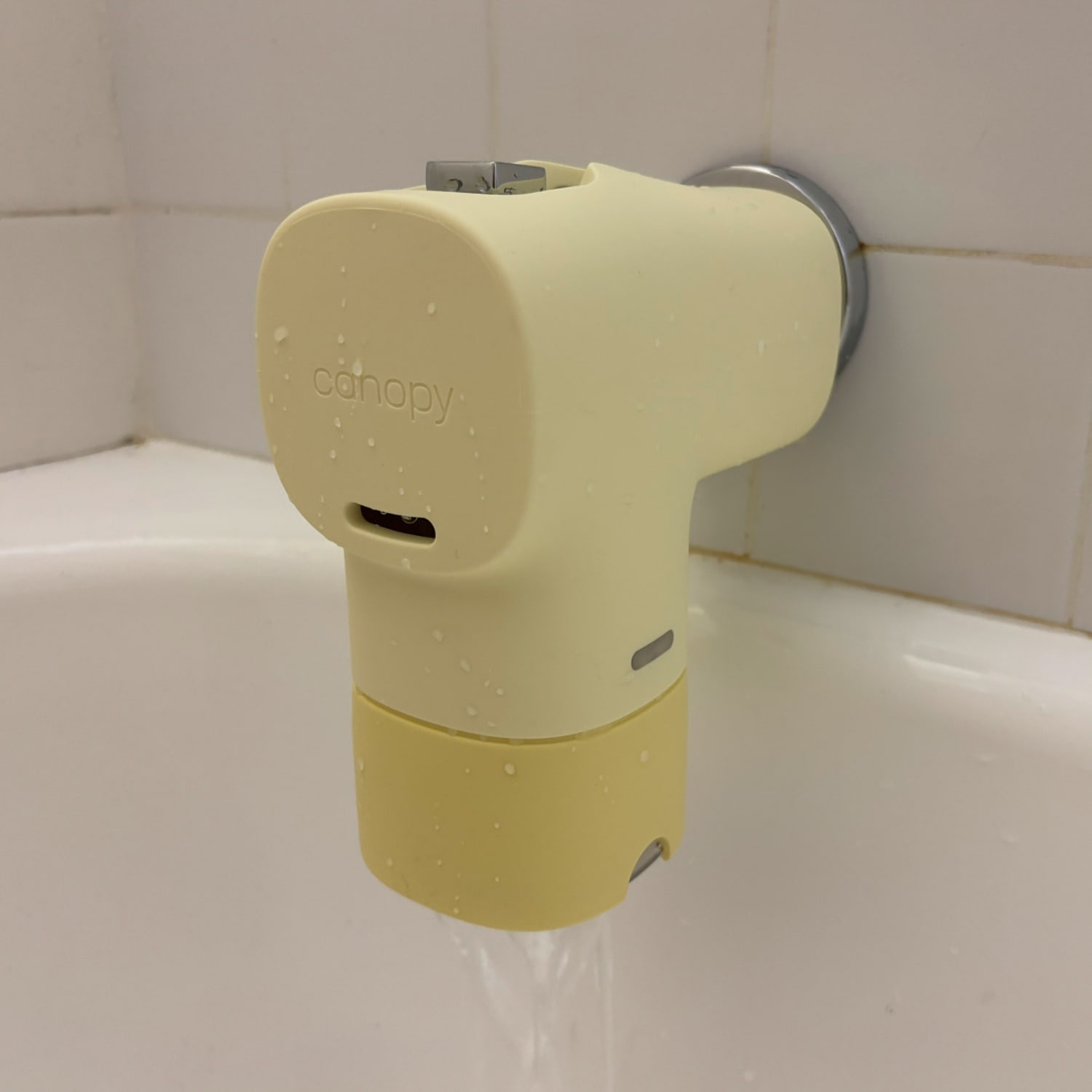 A yellow Canopy Bath Tub Filter installed on a tub spout against a white tile background. (Courtesy Zoe Malin)