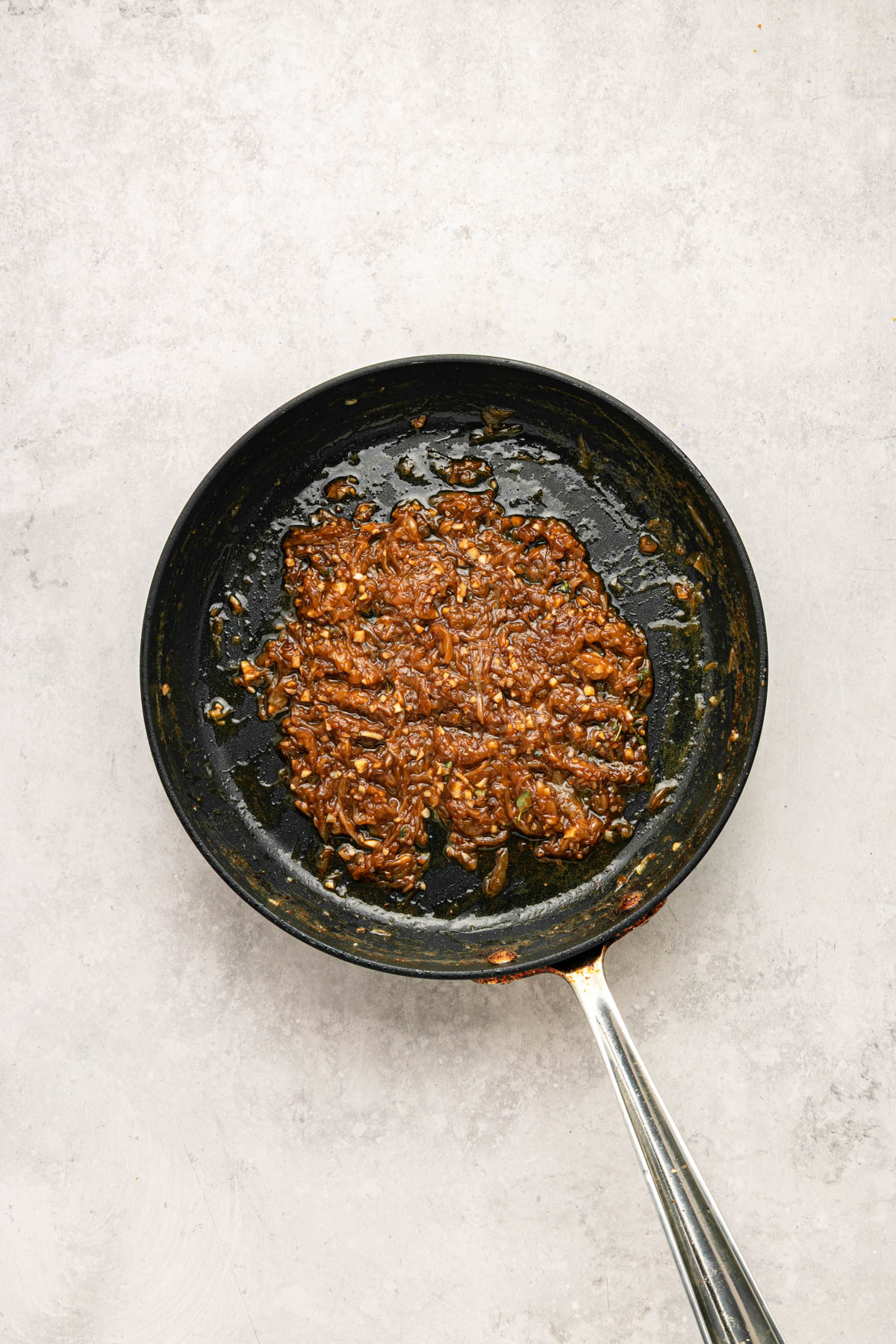 A black frying pan with a cooked mixture of caramelized onions and spices sits on a light gray surface.