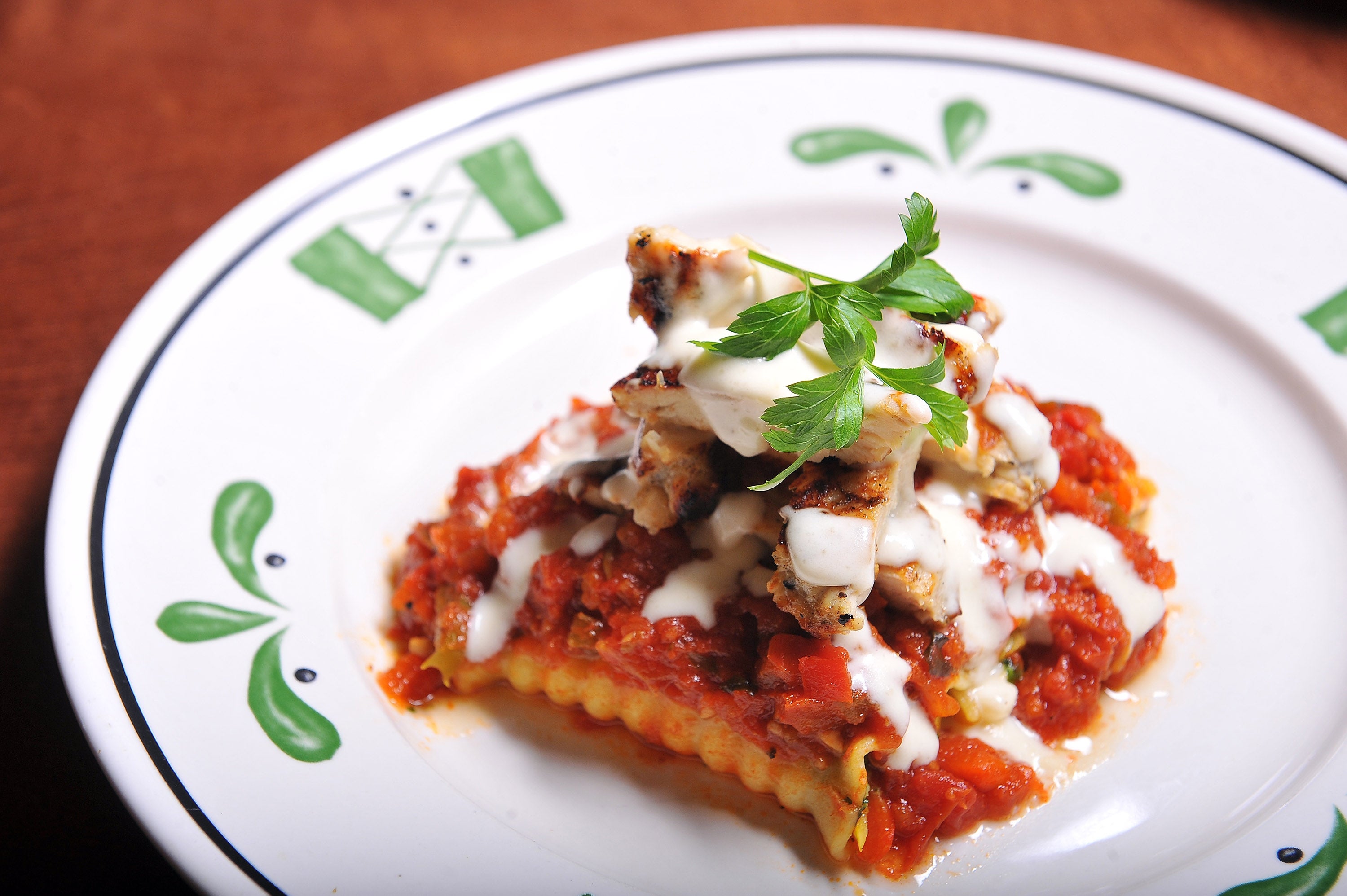 A plate of lasagna topped with sauce and a parsley garnish on patterned dinnerware